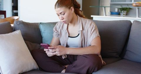 Young woman lounging on sofa scrolling phone in calm minimalist living room