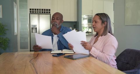 Diverse senior couple reviewing bills and planning finances at kitchen table