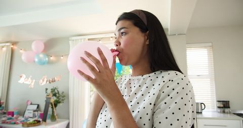 Woman blowing pink balloon for home baby shower party