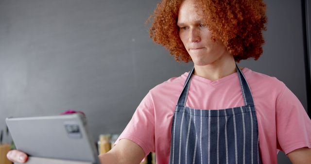Focused biracial man with red curly hair using tablet cooking kitchen. Cooking, food, domestic life, communication and lifestyle, unaltered.