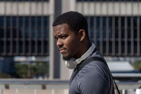 Young Male Commuter Standing on Urban Walkway Wearing Headphones and Backpack in City