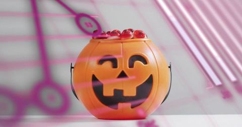 Smiling jack-o'-lantern bucket holding red gummy candies with pink light reflections