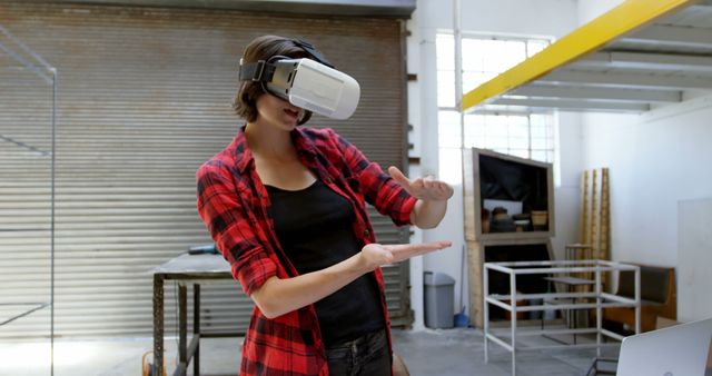 Young woman wearing virtual reality headset in an industrial space, demonstrating and interacting with VR environment. Suitable for use in technology, innovation, and entertainment contexts. Perfect for illustrating immersive experiences, futuristic concepts, and modern tech advancements in a workplace or creative space.