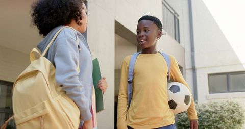 African american teenagers chatting at school entrance with soccer ball and backpacks