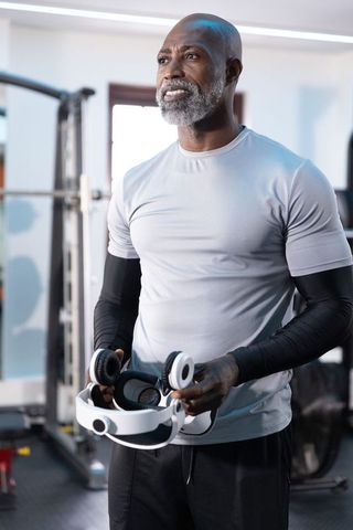Senior african american man holding white vr headset in modern gym wearing arm sleeves