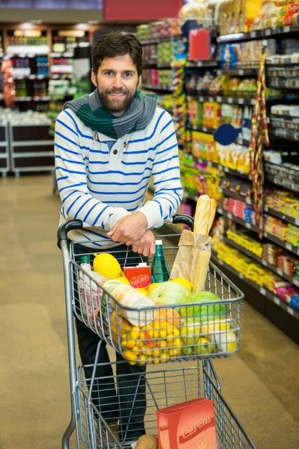 Portrait of smiling man with trolley in grocery section at supermarket