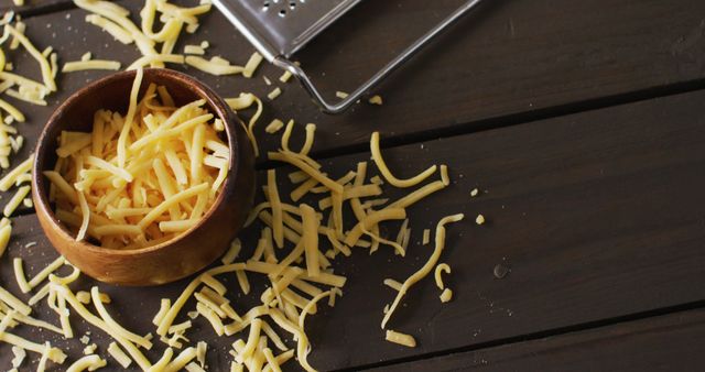 Image of cheese grater and grated cheese in wooden bowl on rustic table with copy space. savoury cooking ingredient and food preparation.