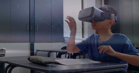Young student wearing vr headset reaching virtual hud while learning at classroom desk