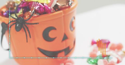 Jack-o-lantern bucket filling with assorted halloween candy and decorative spider closeup