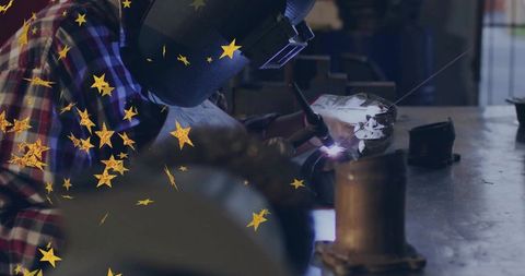 Welder wearing protective helmet welding metal at workbench with decorative gold stars