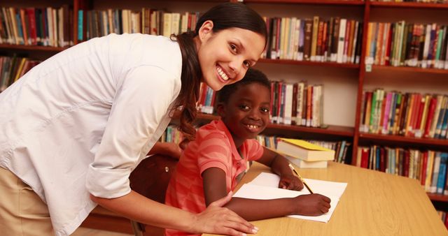 Teacher helping pupil and smiling at camera in library - Download Free Stock Photos Pikwizard.com