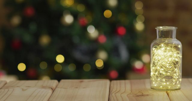Image of wooden table with fairy lights in jar over defocussed christmas tree with baubles. . christmas, tradition and celebration concept.