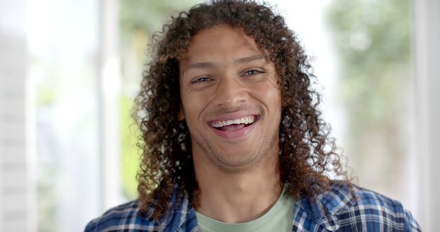 Portrait of happy biracial man with long curly dark hair smiling at home. Domestic life and lifestyle, unaltered.