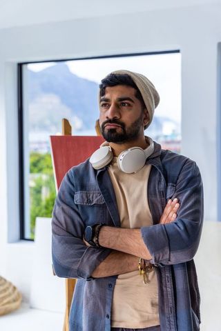 Indian artist standing by window contemplating red canvas in minimalist studio