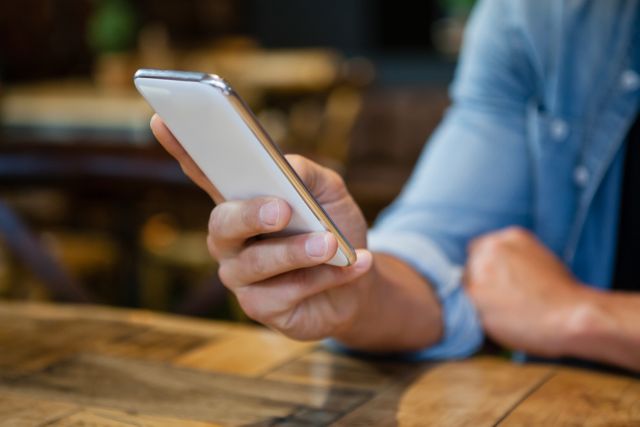 Cropped image of man using smart phone while sitting at table in cafe