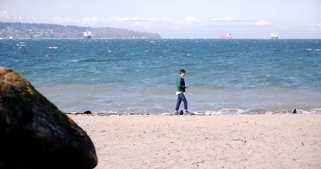 Person walking alone on a sandy beach during daytime with ships in the distance. Ideal for themes of solitude, relaxation, beach activities, and coastal landscapes. Suitable for travel blogs, nature articles, and promotional materials for seaside destinations.