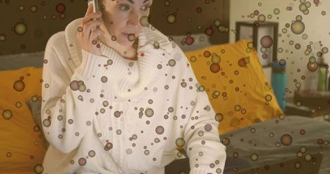 Young woman multitasking on laptop and phone in cozy bedroom with abstract bubble overlay