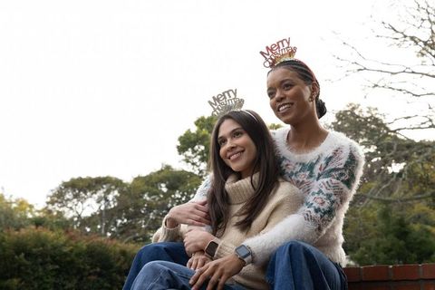 Friends embracing on brick wall wearing merry christmas headbands and cozy knit sweaters