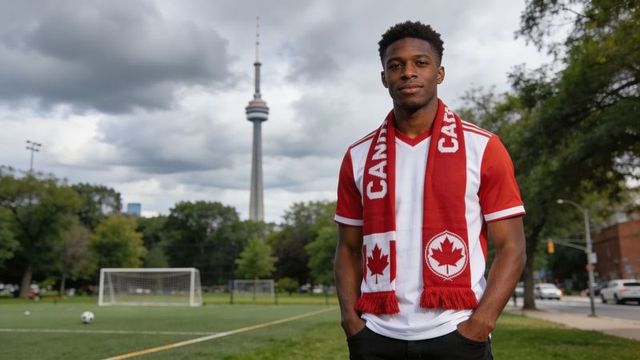 Young fan wearing canada scarf and jersey standing on toronto soccer pitch with cn tower