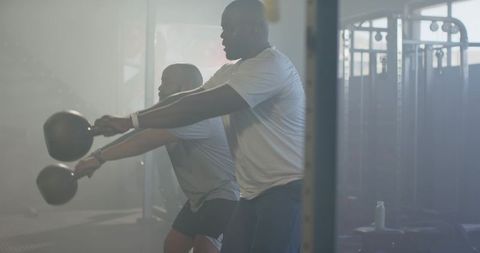 African men performing kettlebell swings for partner strength training in gym facility