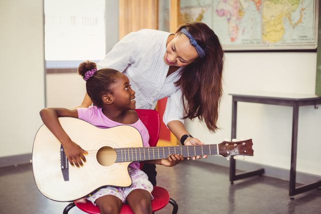 Teacher assisting a girl to play a guitar in classroom at school
