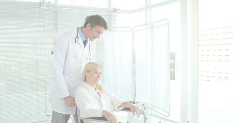 Clinician assisting patient in wheelchair during clinic consultation in bright medical room