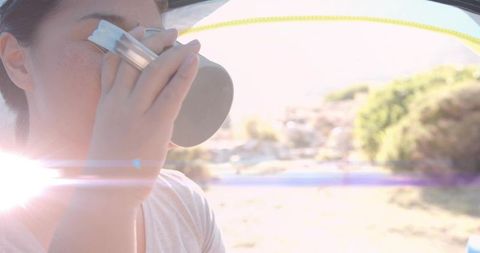 Woman drinking from metal camping mug near tent on sunny day