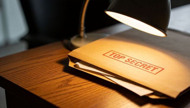 Manila folder stamped TOP SECRET on wooden desk under angled lamp creating moody work scene
