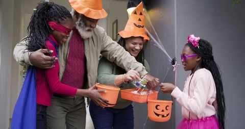 Family sharing halloween candy with costumed children on porch while trick-or-treating