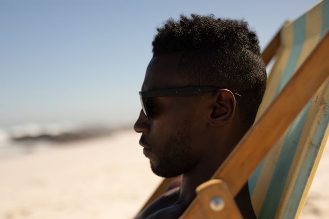 African American man siting in a chair on a beach, wearing sunglasses. Free time and vacation. 