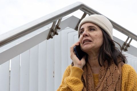 Woman in beanie and mustard sweater talking on phone on urban staircase under overcast sky