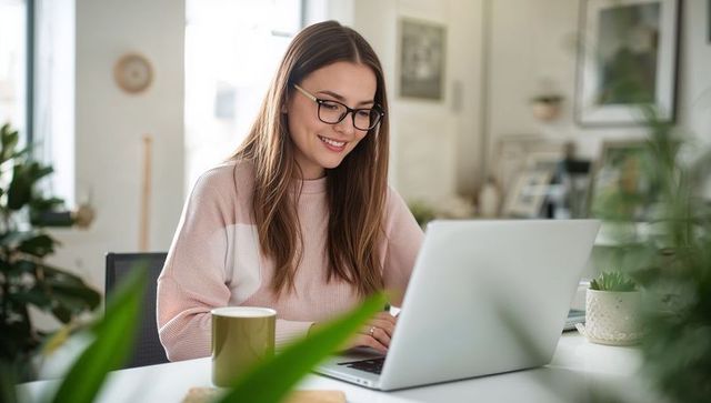 Young woman working from home smiling while typing on laptop at bright cozy modern desk