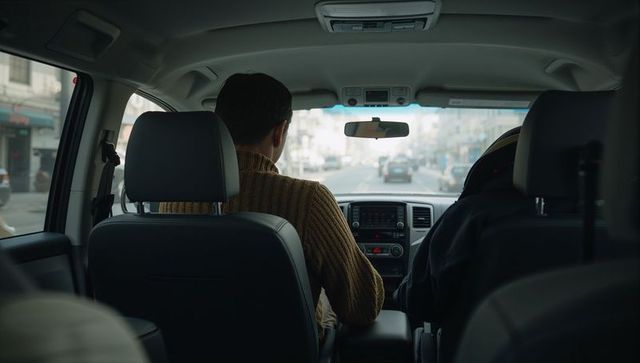 Rear-seat perspective of driver navigating busy city street with dashboard and passenger