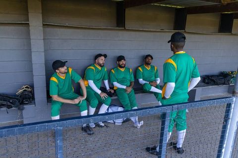 Baseball squad in green and yellow uniforms discussing game strategy in dugout