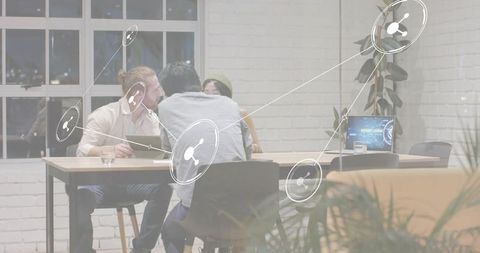 Startup team brainstorming around laptop in biophilic coworking space with network overlay