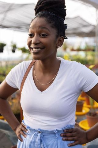 Smiling african american woman shopping plants in greenhouse wearing white v-neck headband