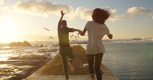 Romantic diverse couple holding hands and running on pier at sunrise, copy space - Download Free Stock Photos Pikwizard.com