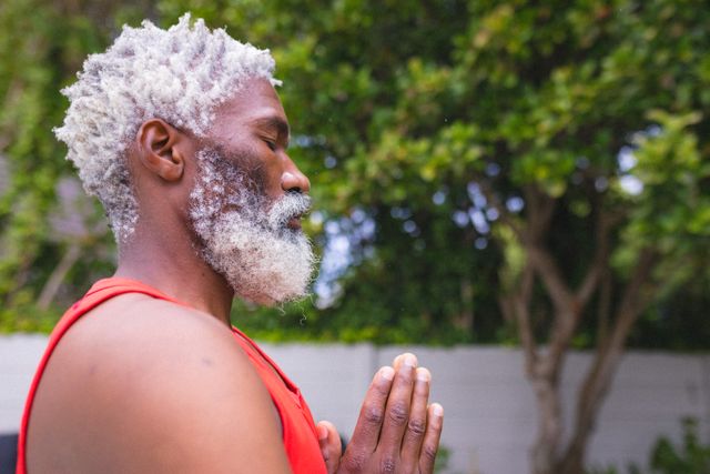 White bearded african american senior man practicing yoga while meditating with hands clasped. unaltered, people, fitness and active lifestyle concept.