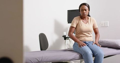 Anxious patient sitting on clinic exam table holding thighs waiting for consultation