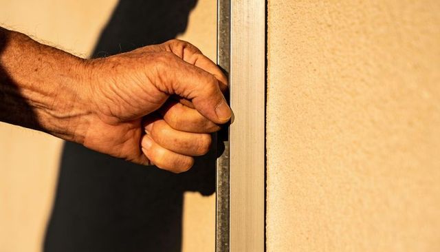 Sunlit gripping male hand holding metal rail against stucco wall closeup