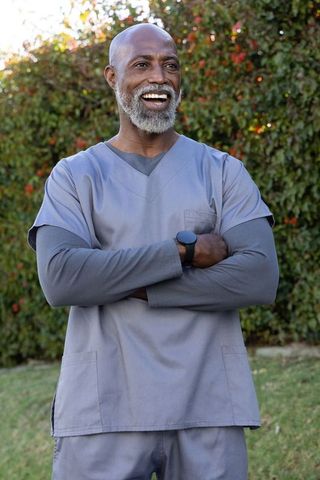 African american senior nurse smiling outdoors in gray scrubs showing smartwatch, confident