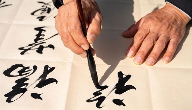 Elderly hands creating traditional ink calligraphy with brush on rice paper
