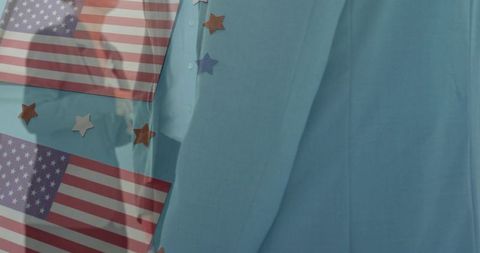 Window reflection of person in light blue jacket with american flags and star decorations