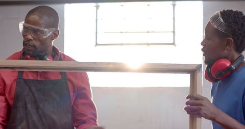 Coworkers collaborating in woodshop with safety equipment