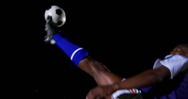 A soccer player is captured in action during a night game, with a focus on the leg striking the ball. Dynamic lighting emphasizes the motion and energy of the sport.