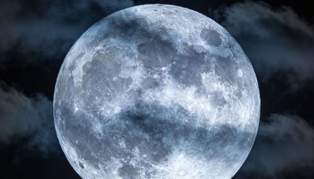 Gibbous moon glowing in blue night sky with detailed craters and wispy clouds