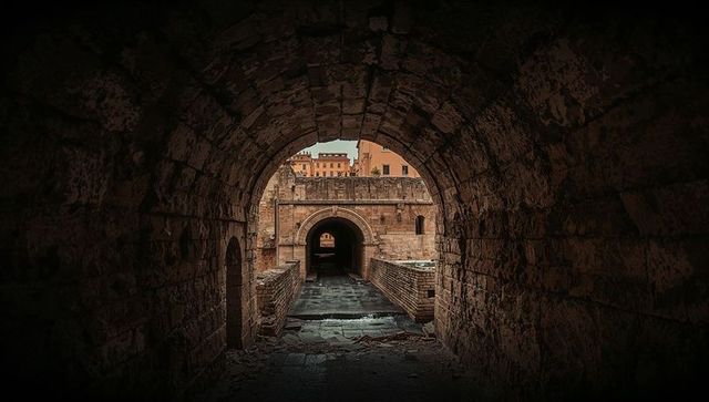 Framing arched tunnel revealing layered stone passage with puddles at historic urban ruins