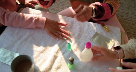 Friends applying neon green manicure in sunlit home salon, relaxed weekend beauty