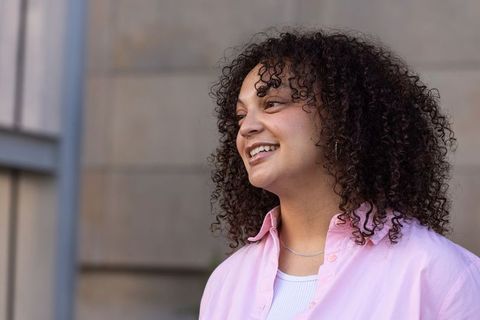 African american woman smiling looking left with curly hair, pastel shirt and necklace