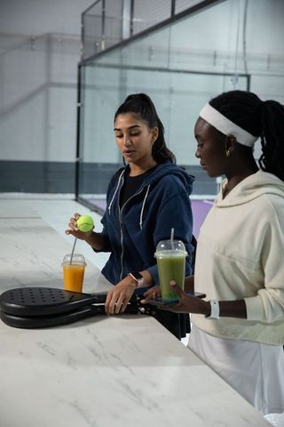 South asian and black friends preparing for padel match holding paddles and smoothies